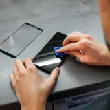Osoba czyści ekran telefonu przed nałożeniem folii hydrożelowej. Obok leży nowa folia.