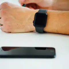 Czarny smartwatch na nadgarstku i leżący obok smartfon. Dowiedz się, jak włączyć bluetooth w zegarku, by połączyć go z telefonem.