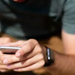 Dłonie trzymające smartfon, na nadgarstku widoczny smartwatch.