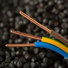 Trzy miedziane żyły kabla elektrycznego, izolowane brązowym, żółto-zielonym i niebieskim przewodem, na tle granulatów tworzywa sztucznego. Idealne do instalacji IP20.