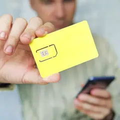 Mężczyzna trzyma żółtą kartę SIM i telefon, pokazując, jak zapisać kontakty na karcie sim.