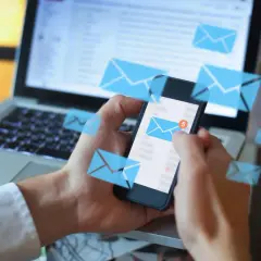 Ręce trzymające smartfon z ikonami wiadomości, obok laptopa. Gdzie jest archiwum SMS w telefonie?