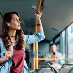 Młoda kobieta w słuchawkach bezprzewodowych trzyma się poręczy w autobusie, słuchając muzyki.