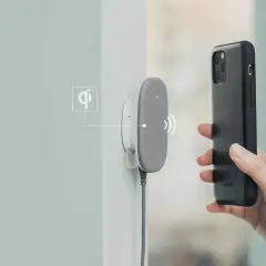 Dłoń zbliża czarne etui z telefonem do szarej ładowarki. Bezprzewodowe ładowanie indukcyjne w akcji.
