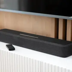 Czarny soundbar z pilotem na białej komodzie, element zestawienia najlepszych soundbarów.