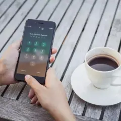Dłoń próbuje odblokować zablokowany iPhone, obok stoi filiżanka kawy.