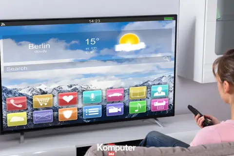 Kobieta z pilotem ogląda nowoczesny telewizor LCD, na którym wyświetla się interfejs z ikonami aplikacji i prognozą pogody dla Berlina.