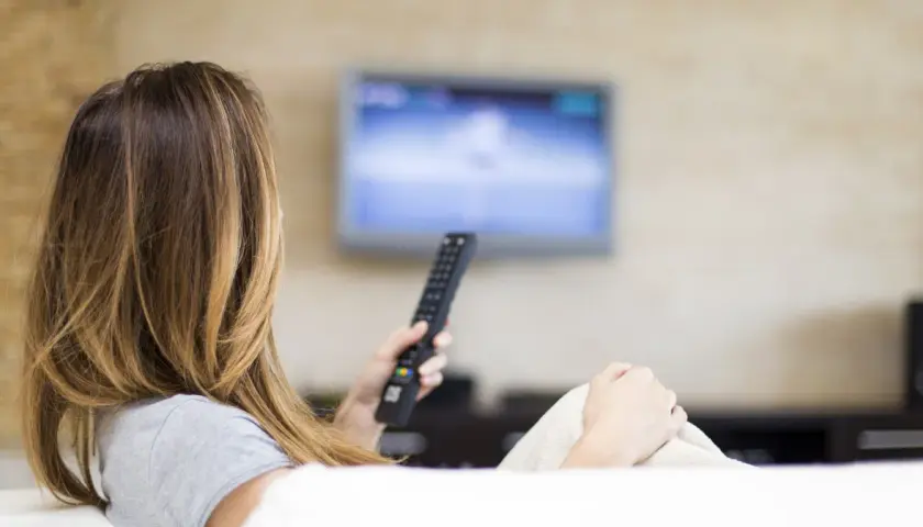 Kobieta z pilotem w ręku ogląda telewizję, ciesząc się swoim abonamentem radiowo-telewizyjnym.