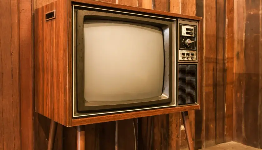 Stary telewizor z drewnianą obudową i ekranem, jak pierwszy telewizor, stoi na tle drewnianej ściany.