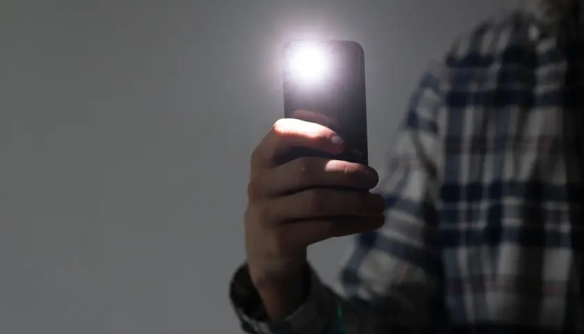 Dłoń trzyma telefon, którego latarka w telefonie rozświetla ciemność.