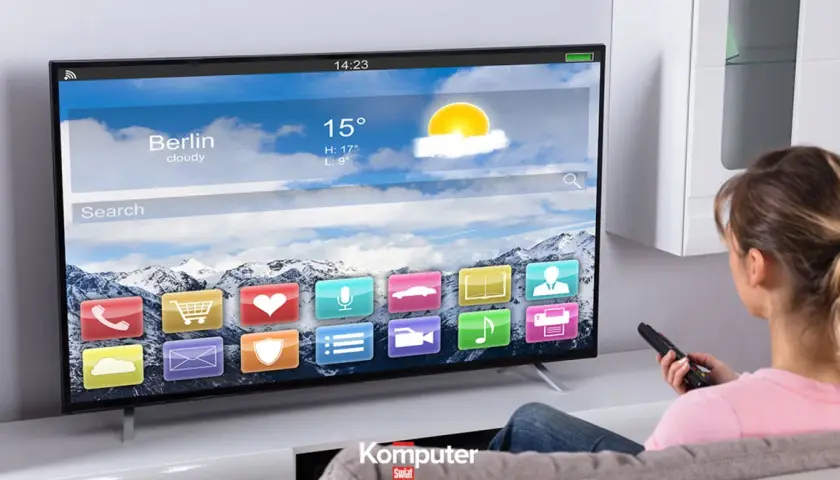 Kobieta z pilotem ogląda nowoczesny telewizor LCD, na którym wyświetla się interfejs z ikonami aplikacji i prognozą pogody dla Berlina.