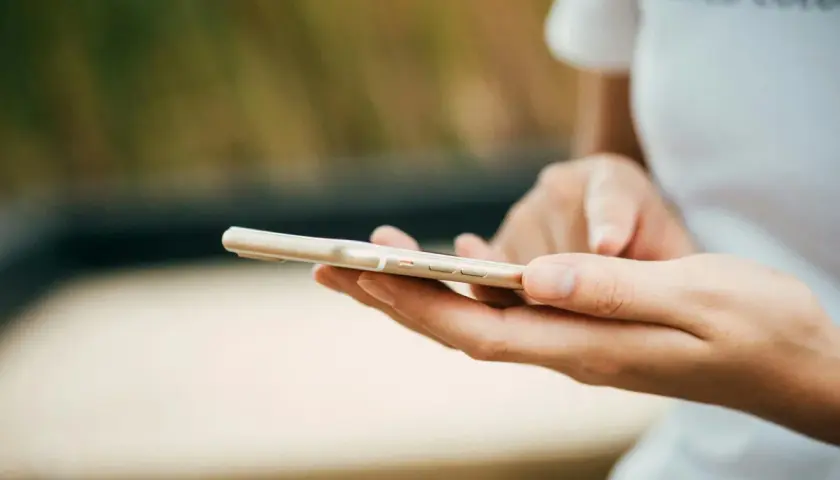 Dłonie trzymające złoty telefon. Zastanawiasz się, jak wyczyścić telefon? Oto praktyczny poradnik.