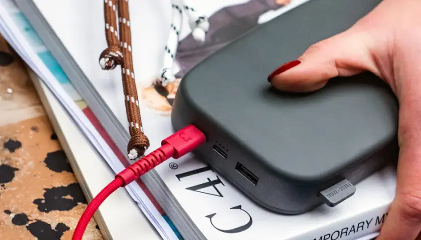 Dłoń z czerwonym lakierem podłącza czerwony kabel do powerbanku, zapewniając szybkie ładowanie.