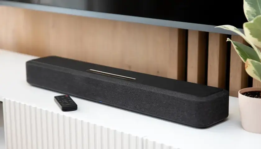 Czarny soundbar z pilotem na białej komodzie, element zestawienia najlepszych soundbarów.