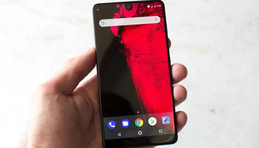 Dłoń trzyma smartfon z wycięciem (notch) na górze ekranu, wyświetlający czerwony wzór i ikonki Androida.