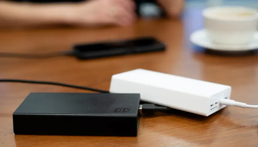 Dwa powerbanki, czarny i biały, leżą na drewnianym stole. W tle widać dłonie i filiżankę kawy. To idealny moment na sprawdzenie powerbank ranking.