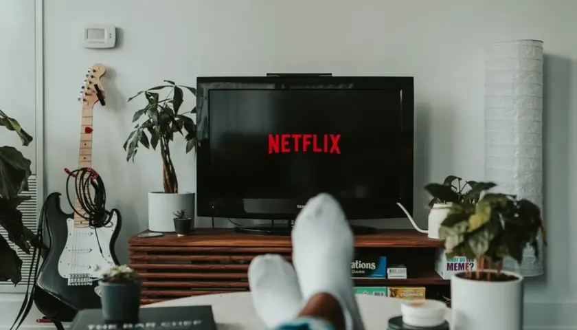 Telewizor z logo Netflix, gitara elektryczna i rośliny w salonie.