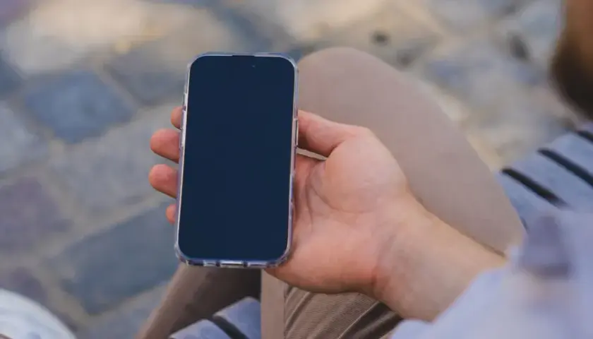 Mężczyzna trzyma iPhone'a w przezroczystym etui. Zastanawia się, jak wyłączyć iPhone'a, aby oszczędzić baterię.