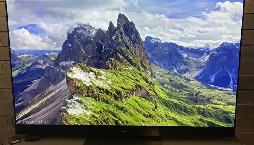 Telewizor wyświetla malowniczy krajobraz górski z zielonymi zboczami i skalistymi szczytami.