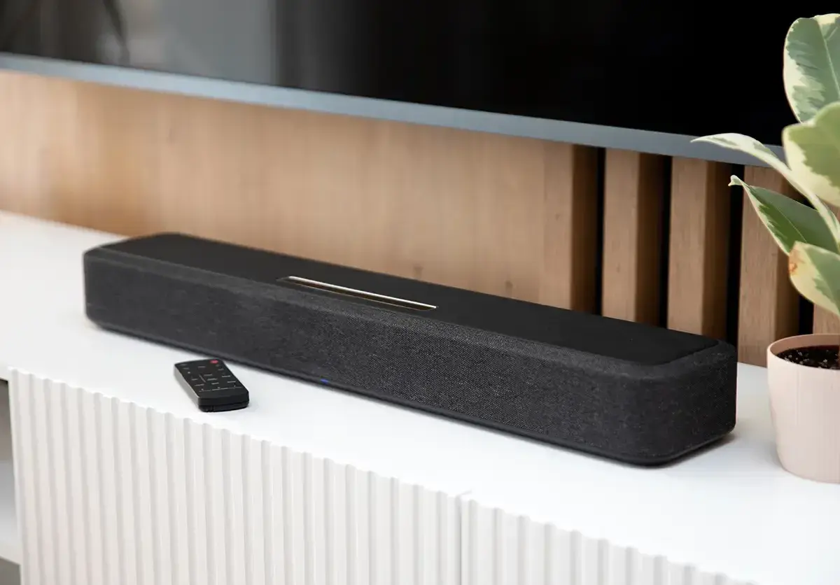 Czarny soundbar z pilotem na białej komodzie, element zestawienia najlepszych soundbarów.