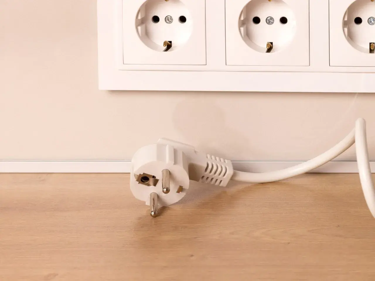 Biała wtyczka typu F leży obok gniazda elektrycznego na drewnianym blacie.