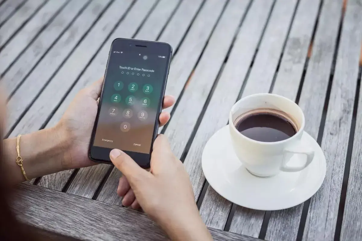 Dłoń próbuje odblokować zablokowany iPhone, obok stoi filiżanka kawy.