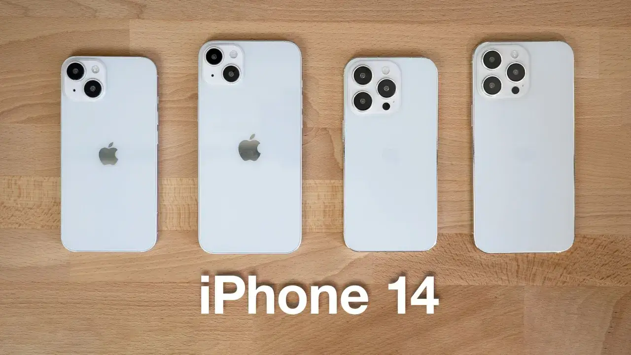 Cztery białe iPhone'y 14 w różnych rozmiarach, od najmniejszego do największego, leżą obok siebie na drewnianym blacie.