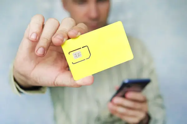 Mężczyzna trzyma żółtą kartę SIM i telefon, pokazując, jak zapisać kontakty na karcie sim.