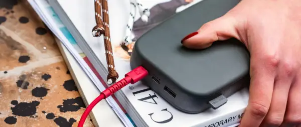 Dłoń z czerwonym lakierem podłącza czerwony kabel do powerbanku, zapewniając szybkie ładowanie.